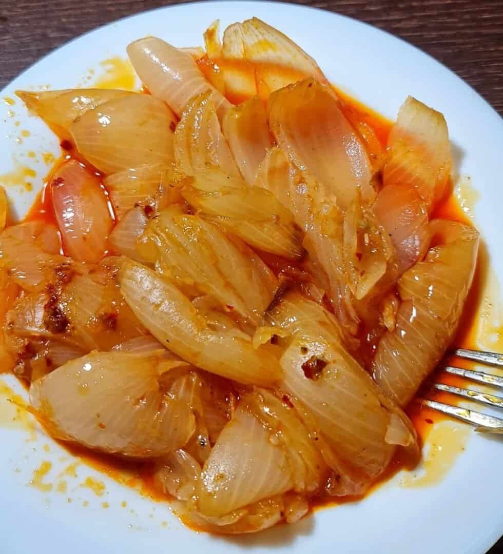 A plate of boiled onions in a spicy red sauce.