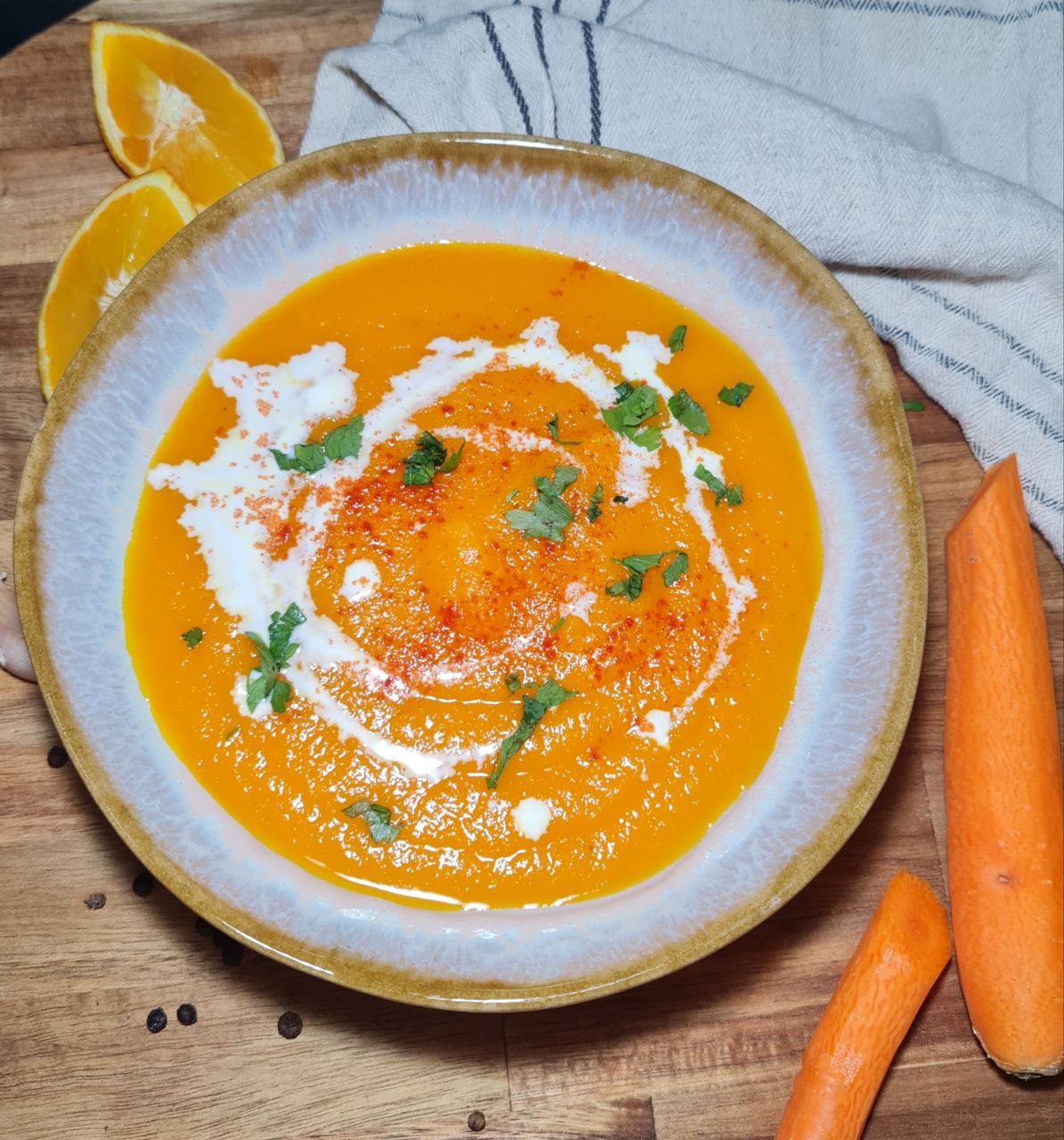 A bowl of vibrant orange carrot soup garnished with a swirl of cream, sprinkled with paprika, and topped with fresh cilantro leaves.