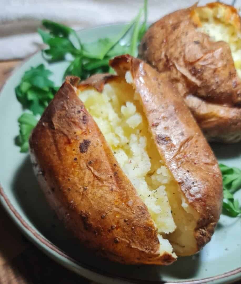 A close-up of a perfectly baked potato with a crispy skin and fluffy interior, served on a plate with a garnish of fresh parsley.