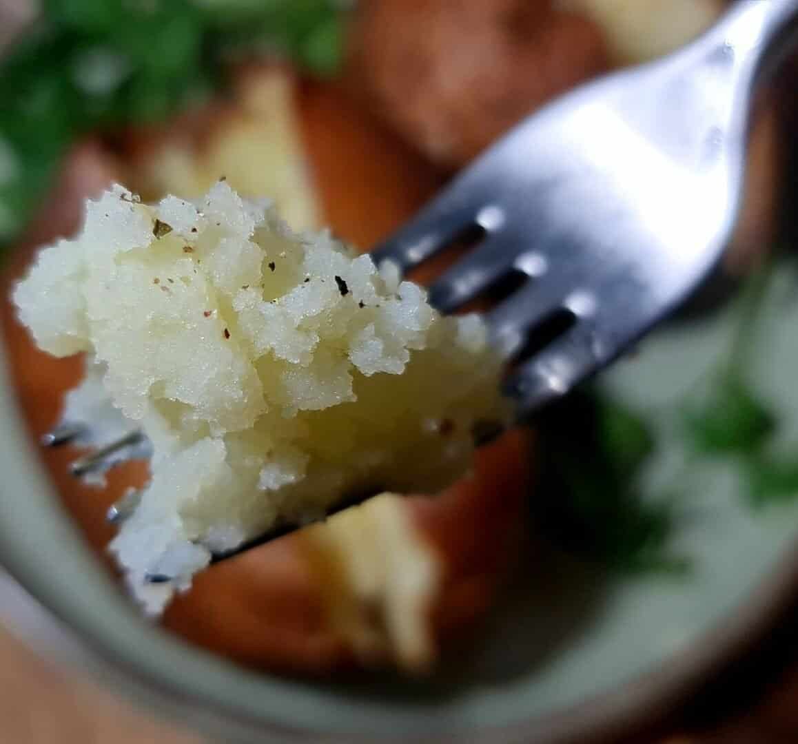  Close-up of a fork holding a bite of fluffy baked potato with seasoning.