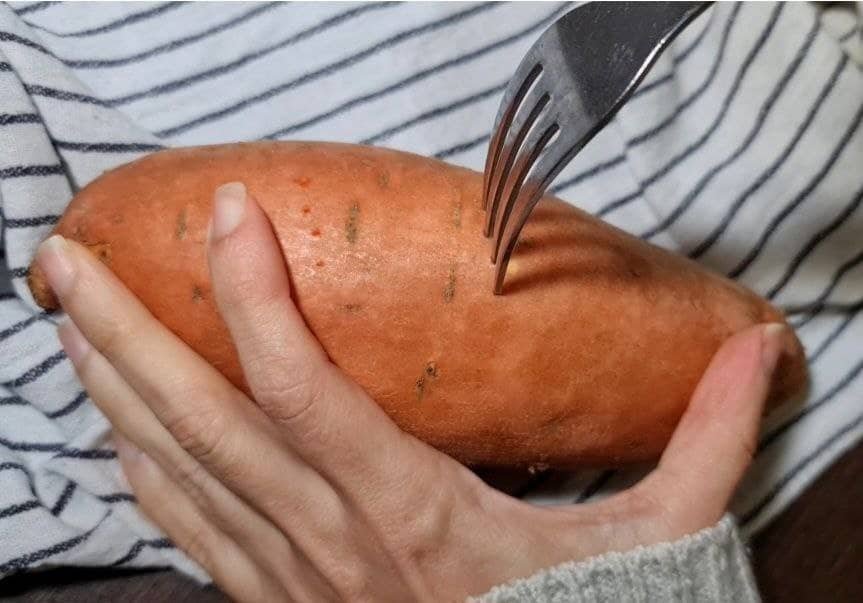 A hand holding a sweet potato while poking it with a fork.