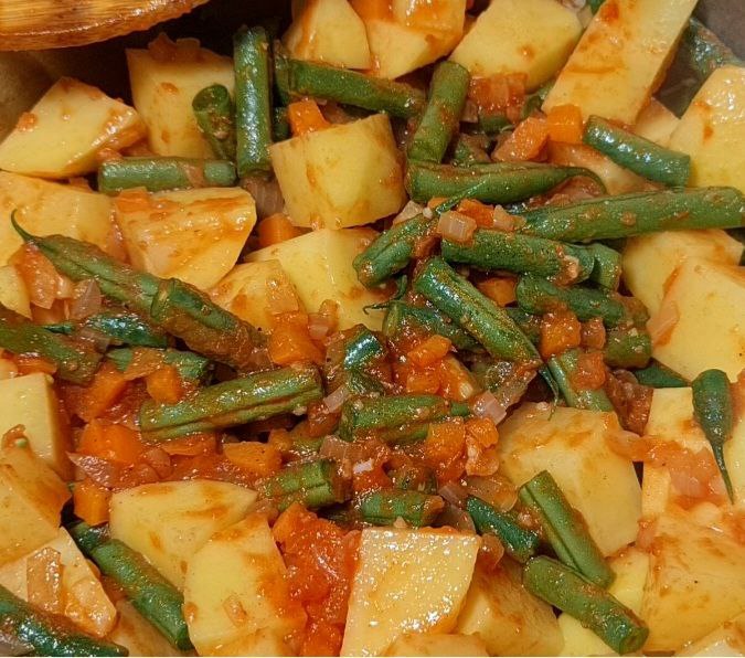 A close-up view of a hearty potato and green beans soup with diced carrots and onions.