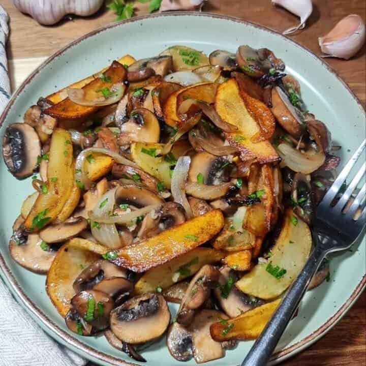 A delicious potato and mushroom skillet with caramelized onions and fresh herbs served on a green plate.