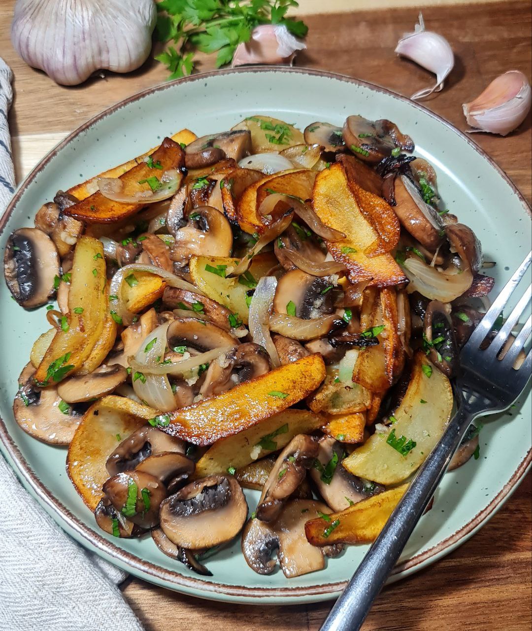 A delicious potato and mushroom skillet with caramelized onions and fresh herbs served on a green plate.