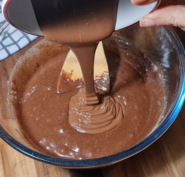 Pouring chocolate mixture into a bowl of vegan brownie batter.