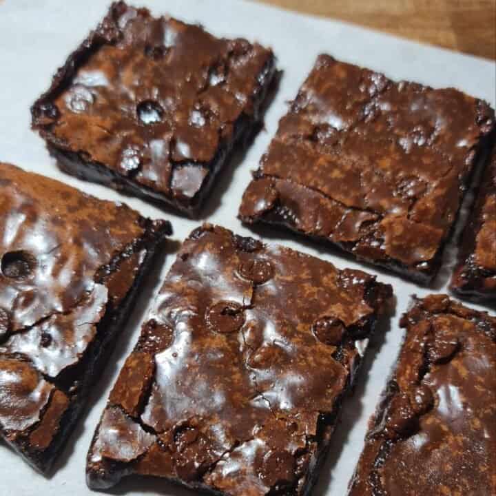 Close-up of six vegan brownies with a shiny, cracked top and rich, fudgy texture.