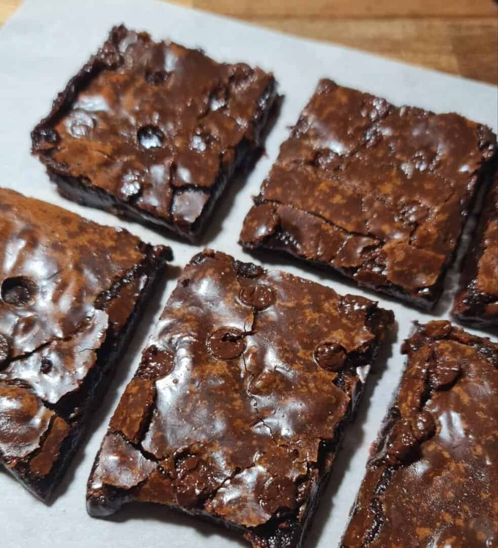 Close-up of six vegan brownies with a shiny, cracked top and rich, fudgy texture.