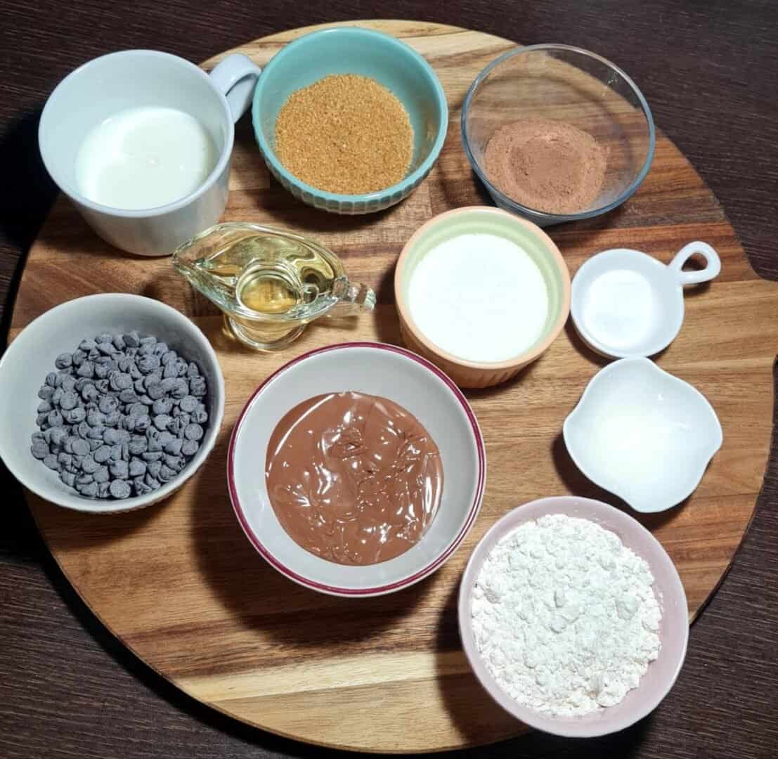 Ingredients for vegan brownies including plant-based milk, brown sugar, cocoa powder, chocolate chips, melted chocolate, flour, oil, baking powder, salt, and vanilla extract.