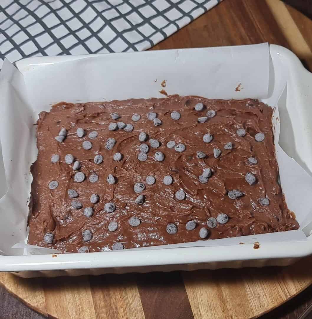 Vegan brownies batter in a white baking dish, topped with chocolate chips, ready to be baked.