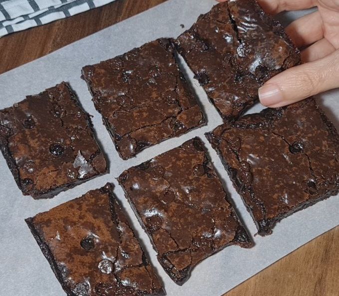 Six pieces of vegan brownies on parchment paper, with a hand picking up one piece.