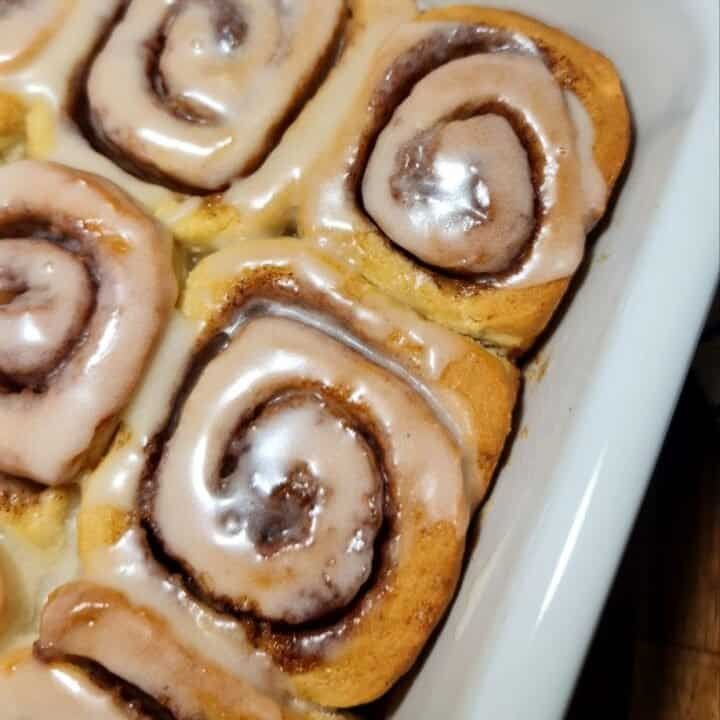 Freshly baked vegan cinnamon rolls with icing in a white baking dish.