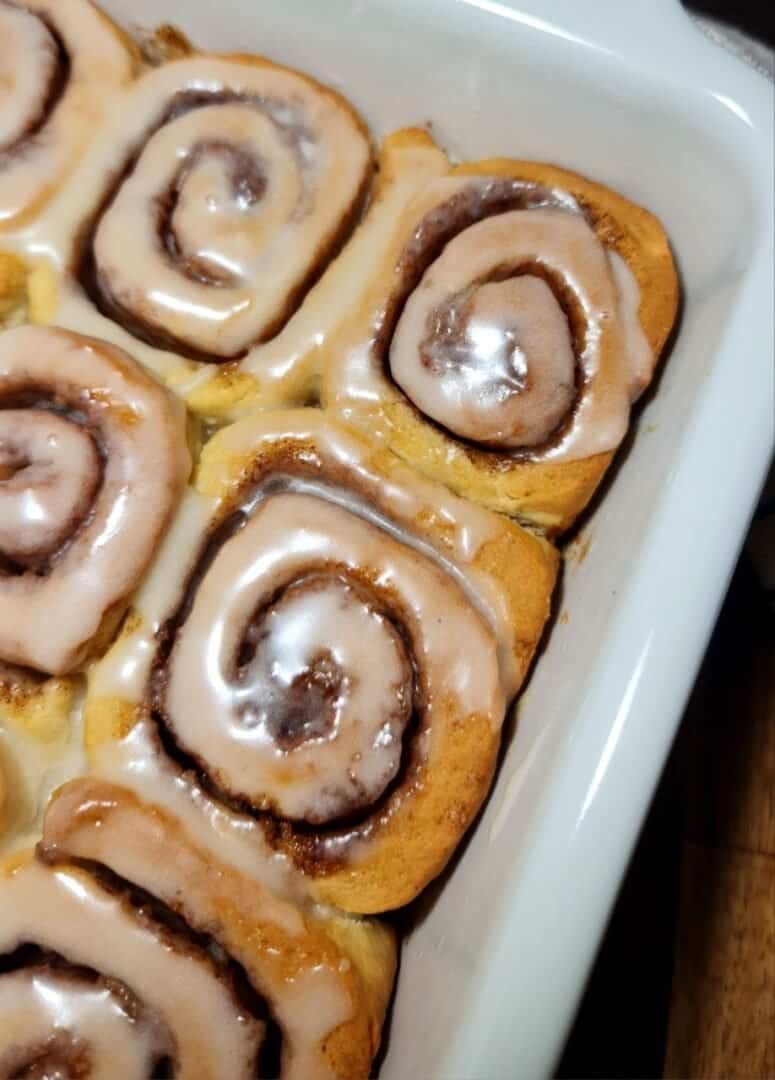  Freshly baked vegan cinnamon rolls with icing in a white baking dish.