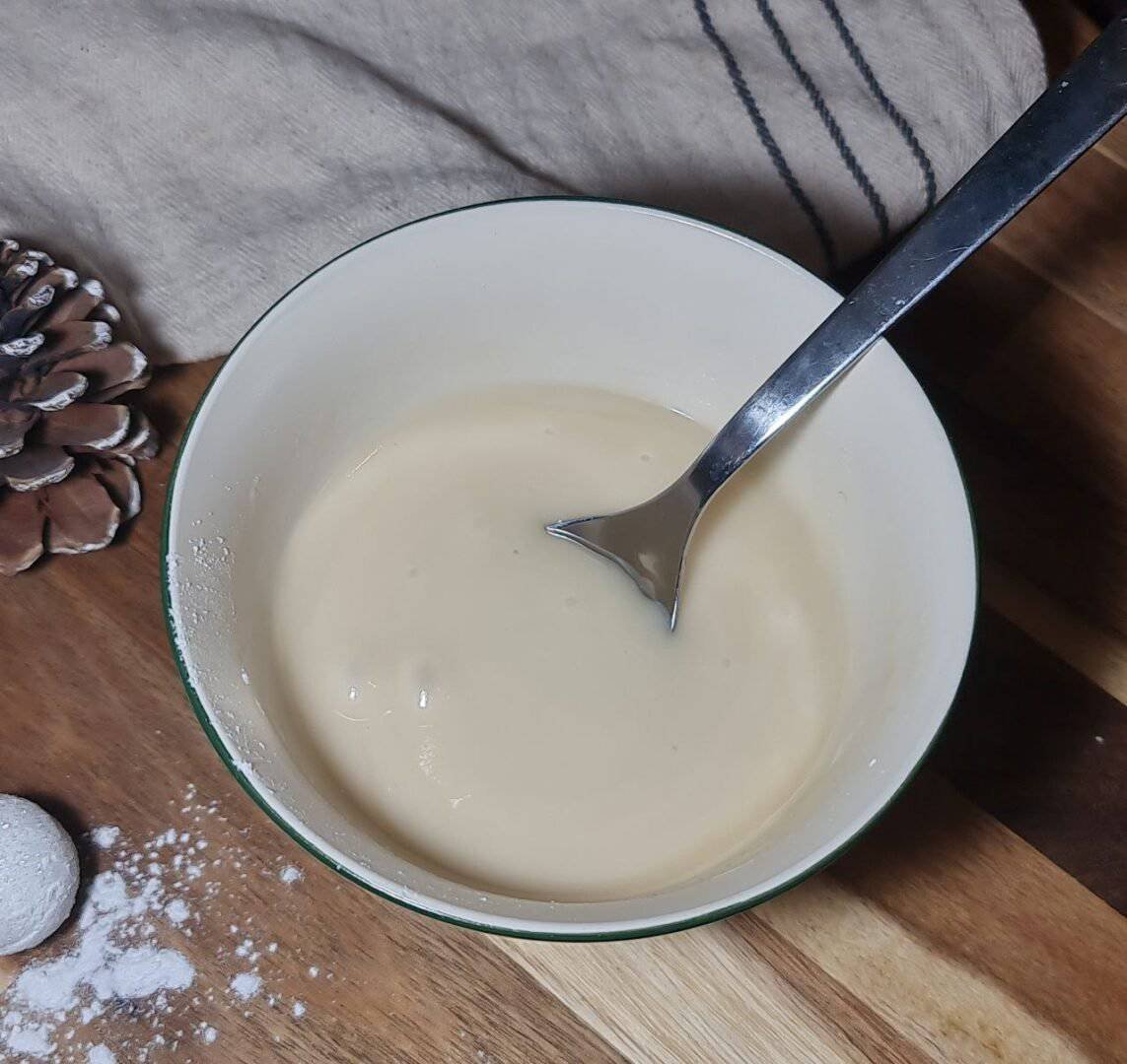  A bowl of creamy vegan icing with a spoon, ready to be used for vegan cinnamon rolls.