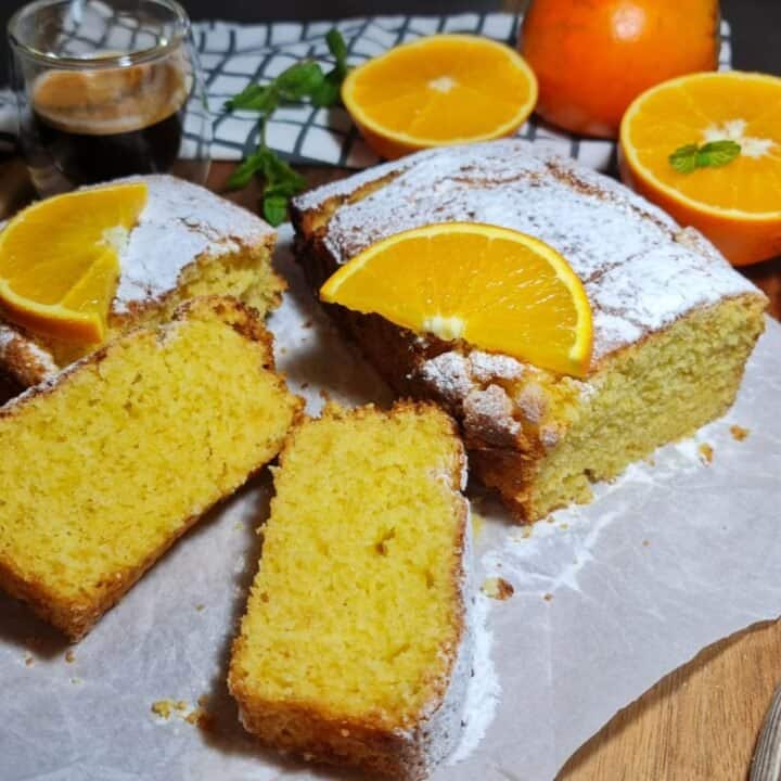 Vegan orange cake topped with powdered sugar and orange slices, served with a cup of espresso.