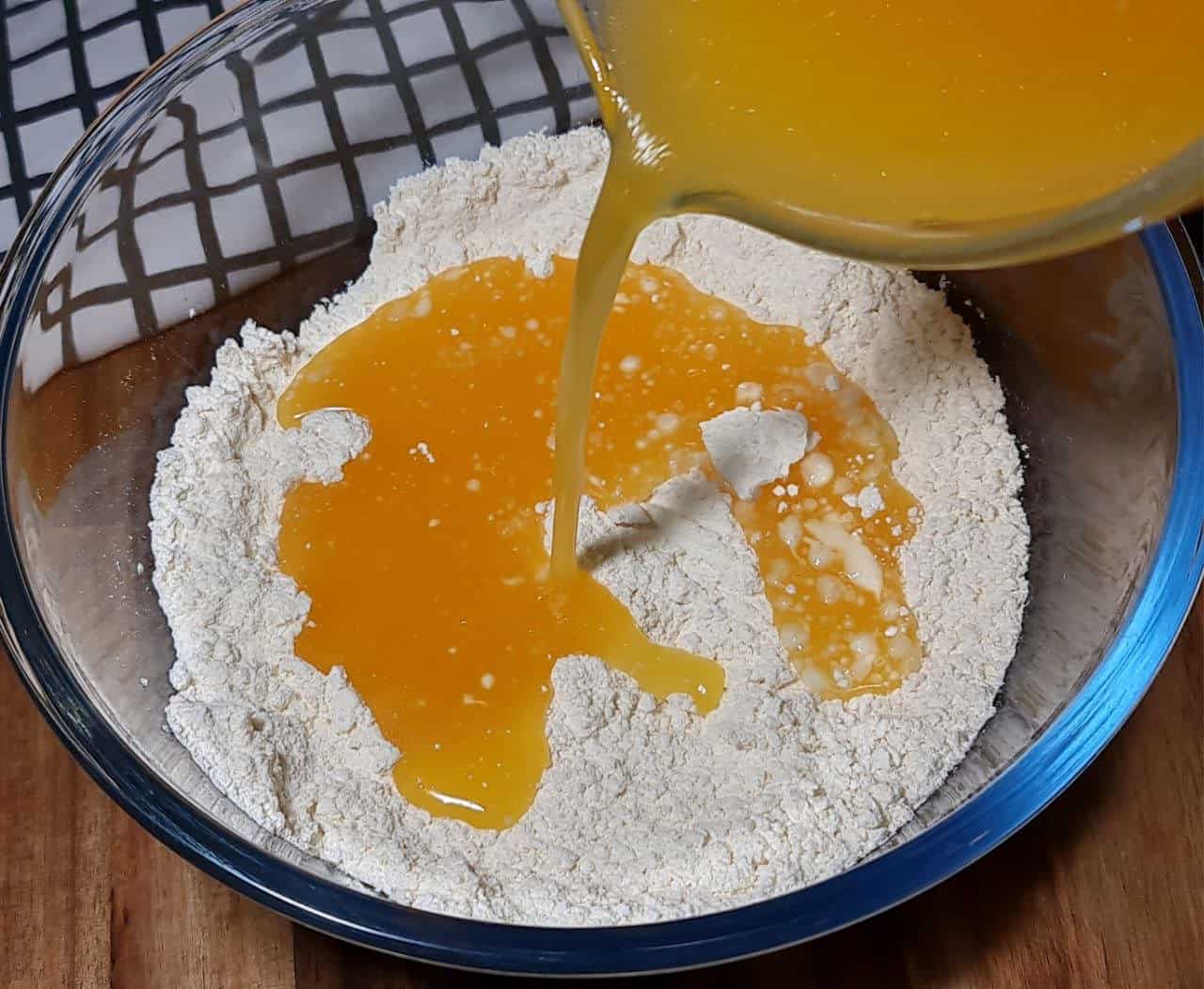 Pouring orange juice into a bowl of flour for vegan orange cake preparation.