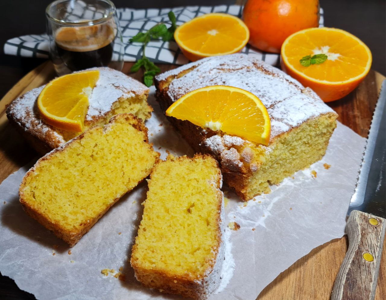 Vegan orange cake topped with powdered sugar and orange slices, served with a cup of espresso.