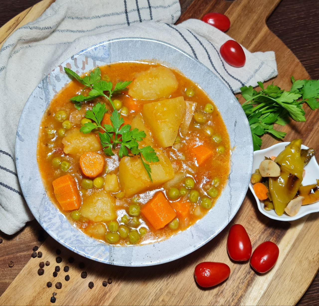 A bowl of vegan peas and potato stew garnished with fresh parsley, featuring chunks of potatoes, carrots, and peas in a rich tomato-based broth.