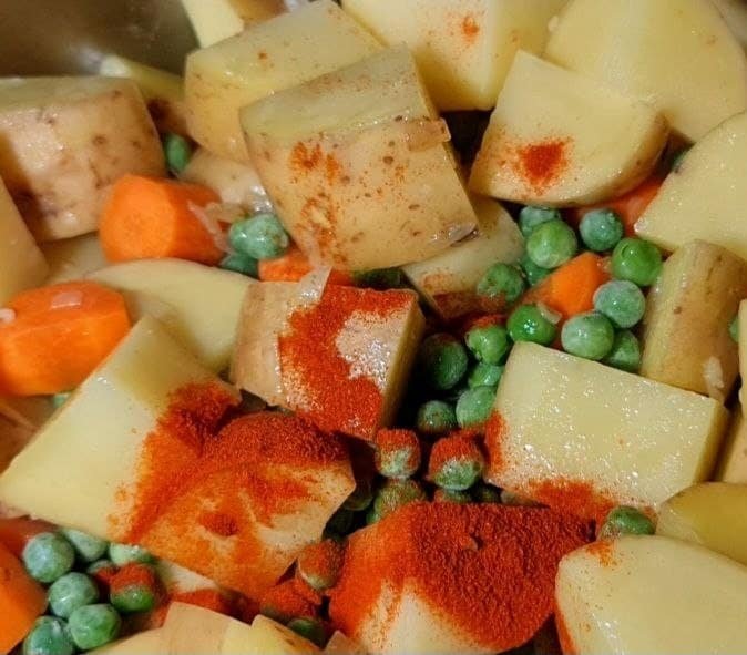  Chopped potatoes, carrots, and peas with paprika seasoning for vegan stew preparation.