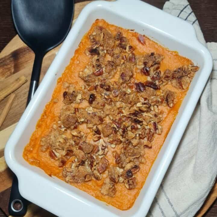 Vegan sweet potato casserole topped with a crunchy pecan and brown sugar crumble in a white baking dish.