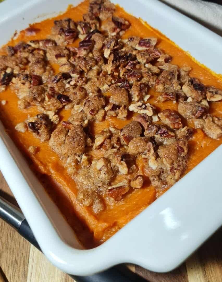 Vegan sweet potato casserole topped with a crunchy pecan and brown sugar crumble in a white baking dish.