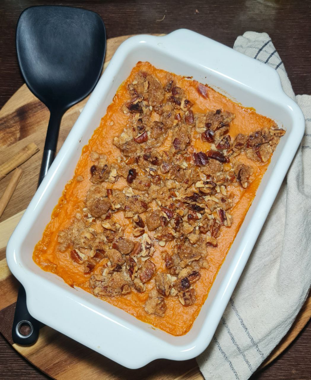 Vegan sweet potato casserole topped with a crunchy pecan and brown sugar crumble in a white baking dish.