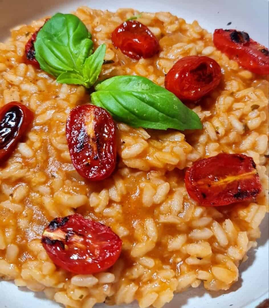 A close-up of a creamy vegan tomato risotto garnished with roasted cherry tomatoes and fresh basil leaves