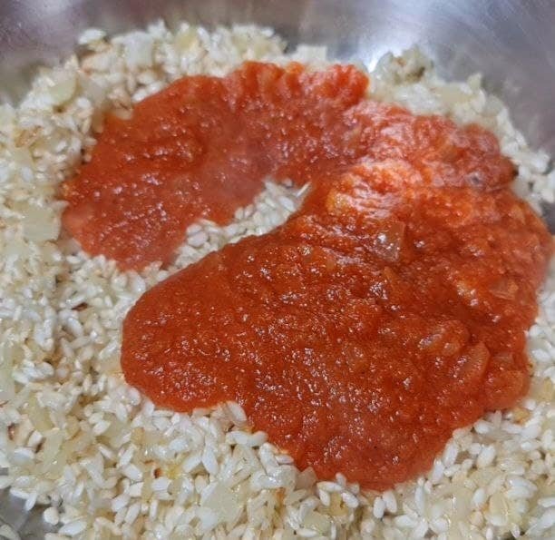 A close-up of a pan with rice and tomato sauce being prepared for vegan tomato risotto.