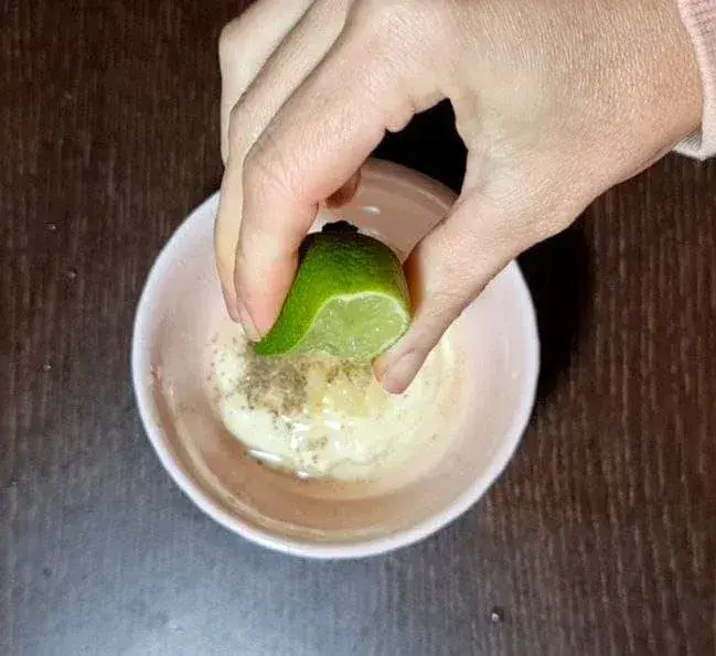 Squeezing lime juice into a bowl of vegan salad dressing ingredients.