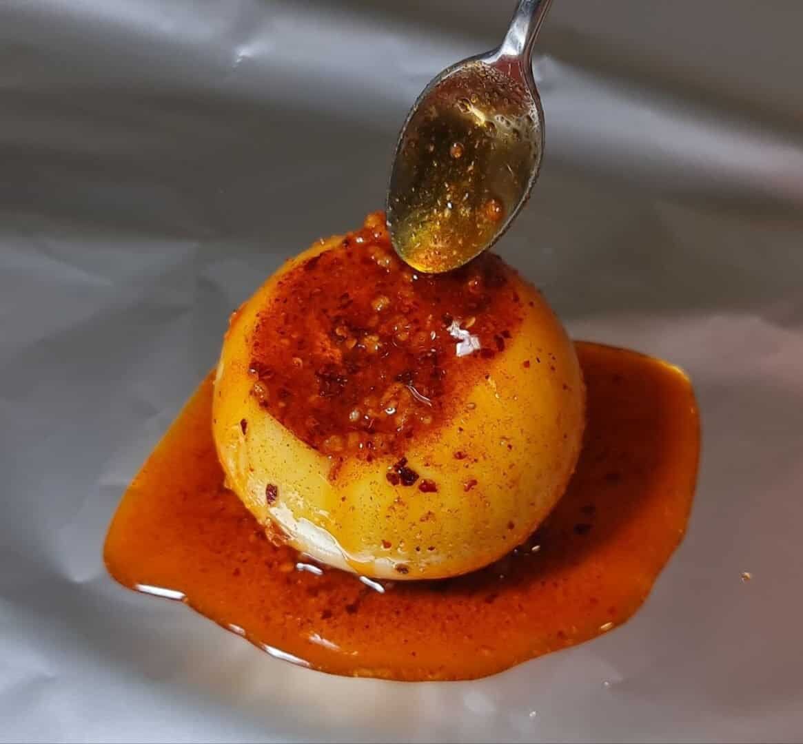 A boiled onion topped with a spicy red sauce being drizzled with more sauce from a spoon.