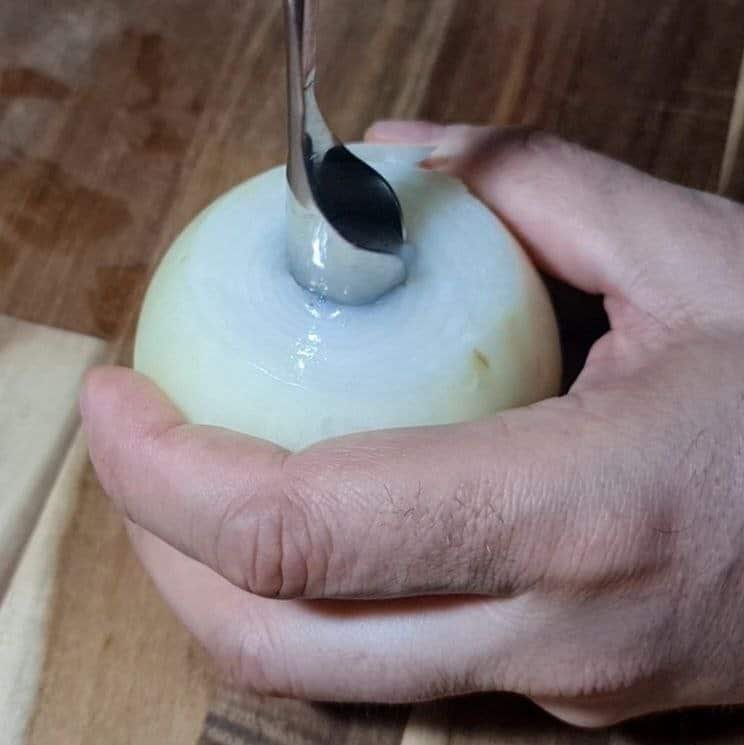 Close-up of a person using a spoon to scoop out the center of an onion.