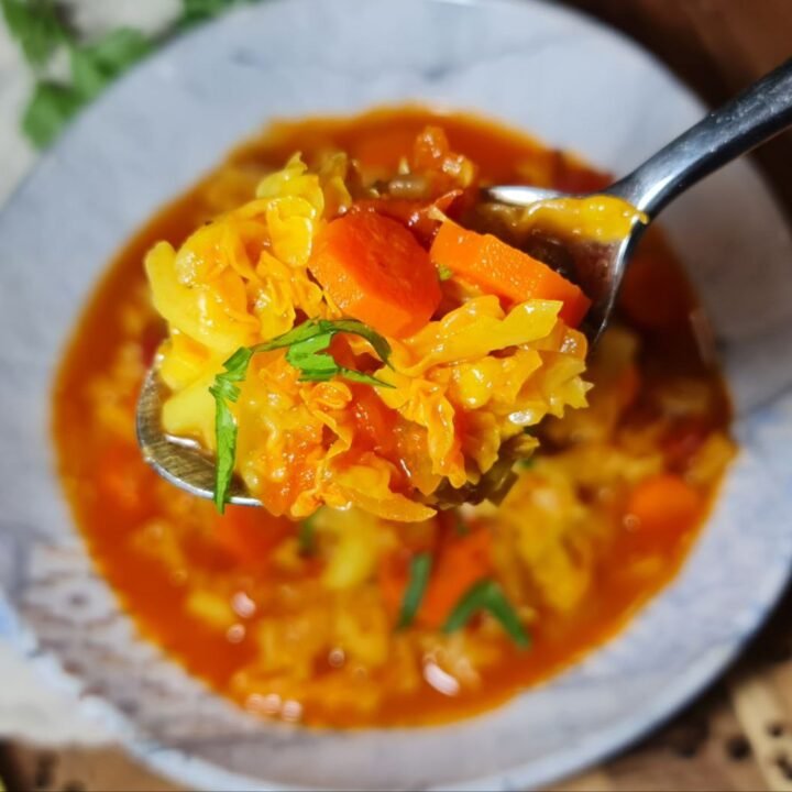 A close-up of a spoonful of vibrant cabbage soup with carrots, tomatoes, and fresh herbs.