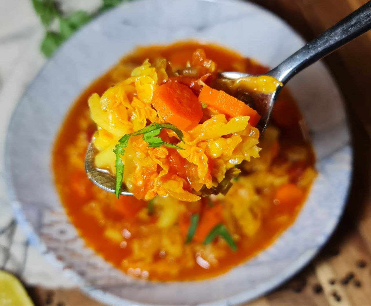  A close-up of a spoonful of vibrant cabbage soup with carrots, tomatoes, and fresh herbs.