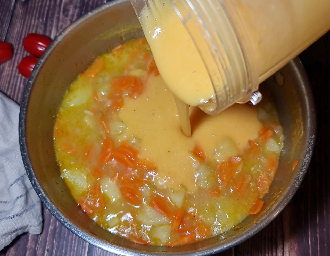 Pouring blended mixture into a pot of carrot and potato soup.