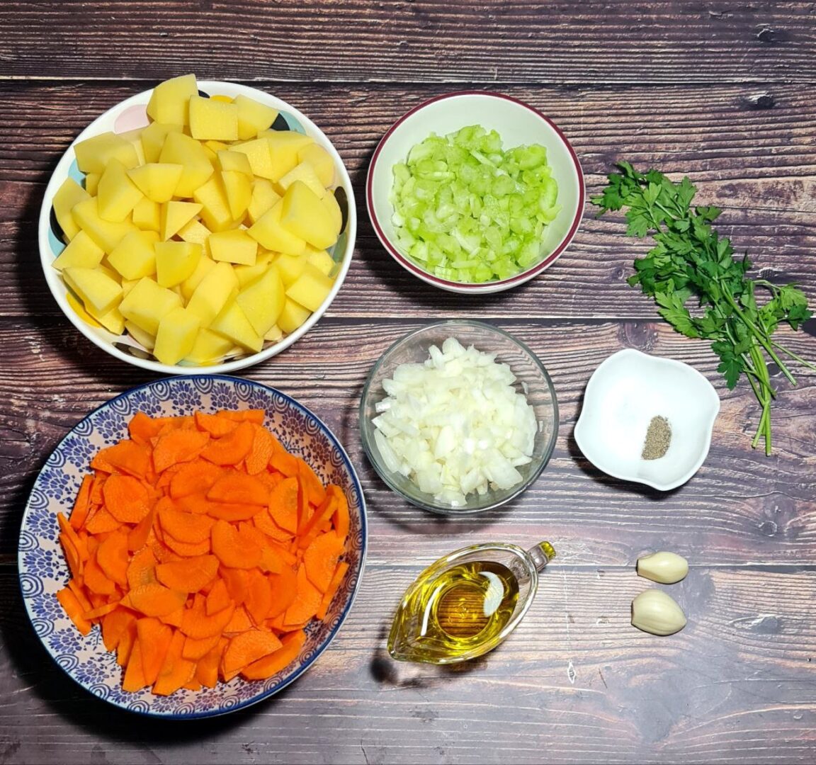 Ingredients for carrot potato soup including chopped carrots, potatoes, celery, onions, garlic, parsley, olive oil, salt, and pepper.