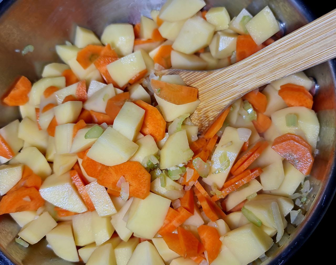 Chopped carrots and potatoes in a pot being stirred with a wooden spoon.