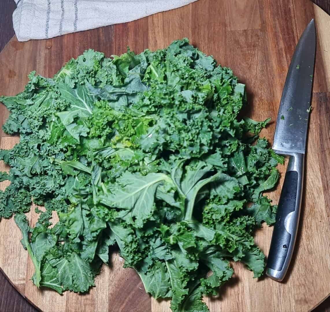 Freshly chopped kale on a wooden cutting board with a knife.