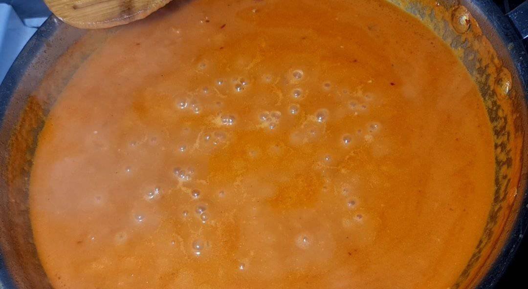 A close-up view of a simmering coconut milk pasta sauce in a pan, showing its rich, creamy texture and vibrant orange color.