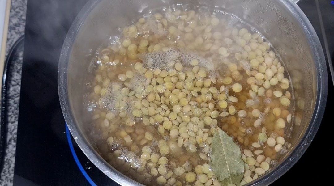 A pot of lentils boiling with a bay leaf on top.