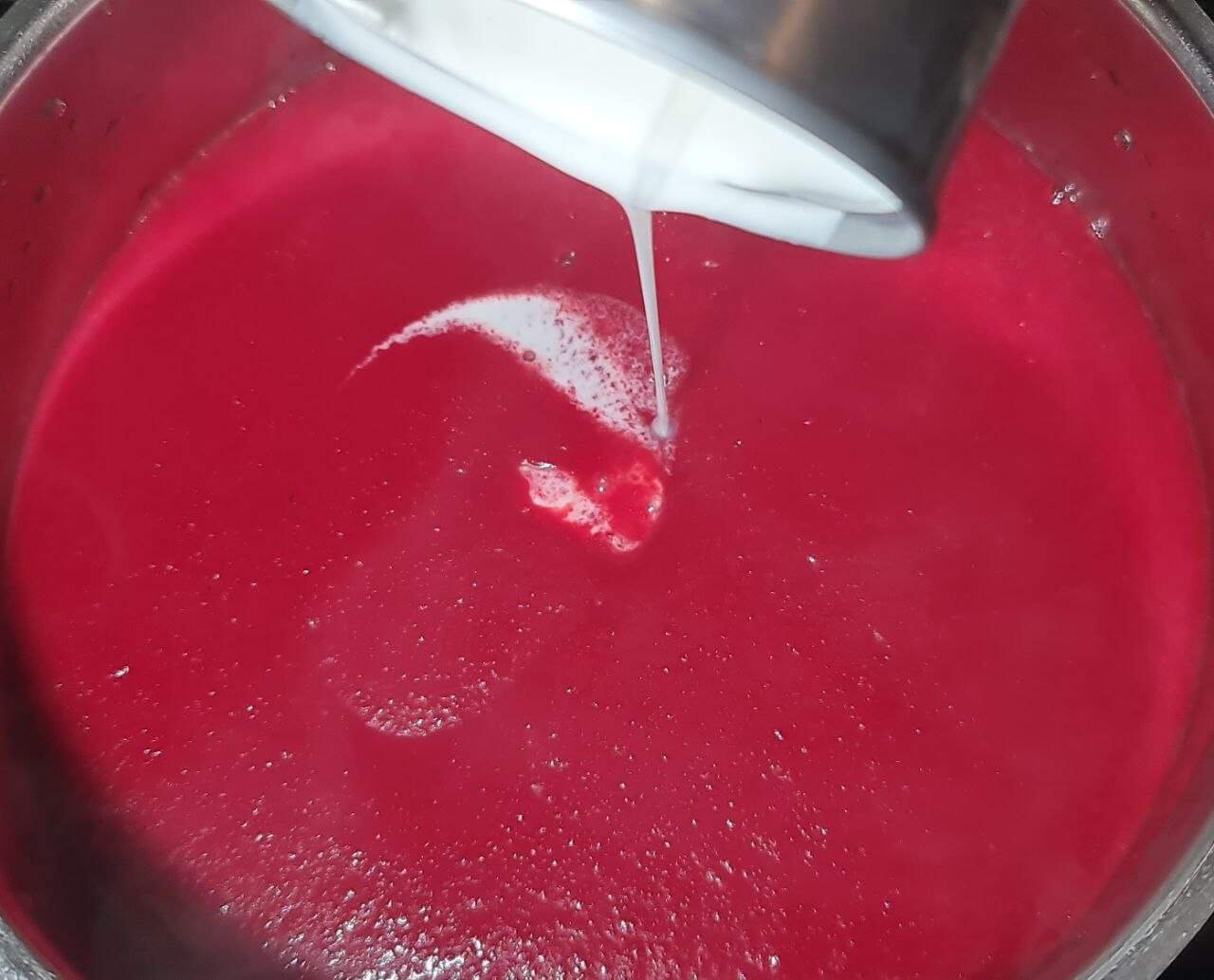 Pouring coconut milk into a pot of vibrant red beet soup.