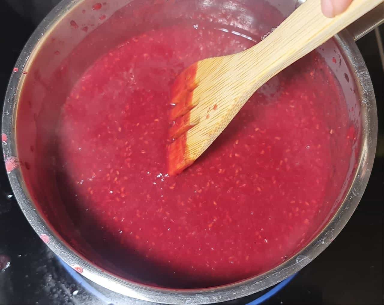 Stirring raspberry sauce in a pot for a guilt-free cake recipe.