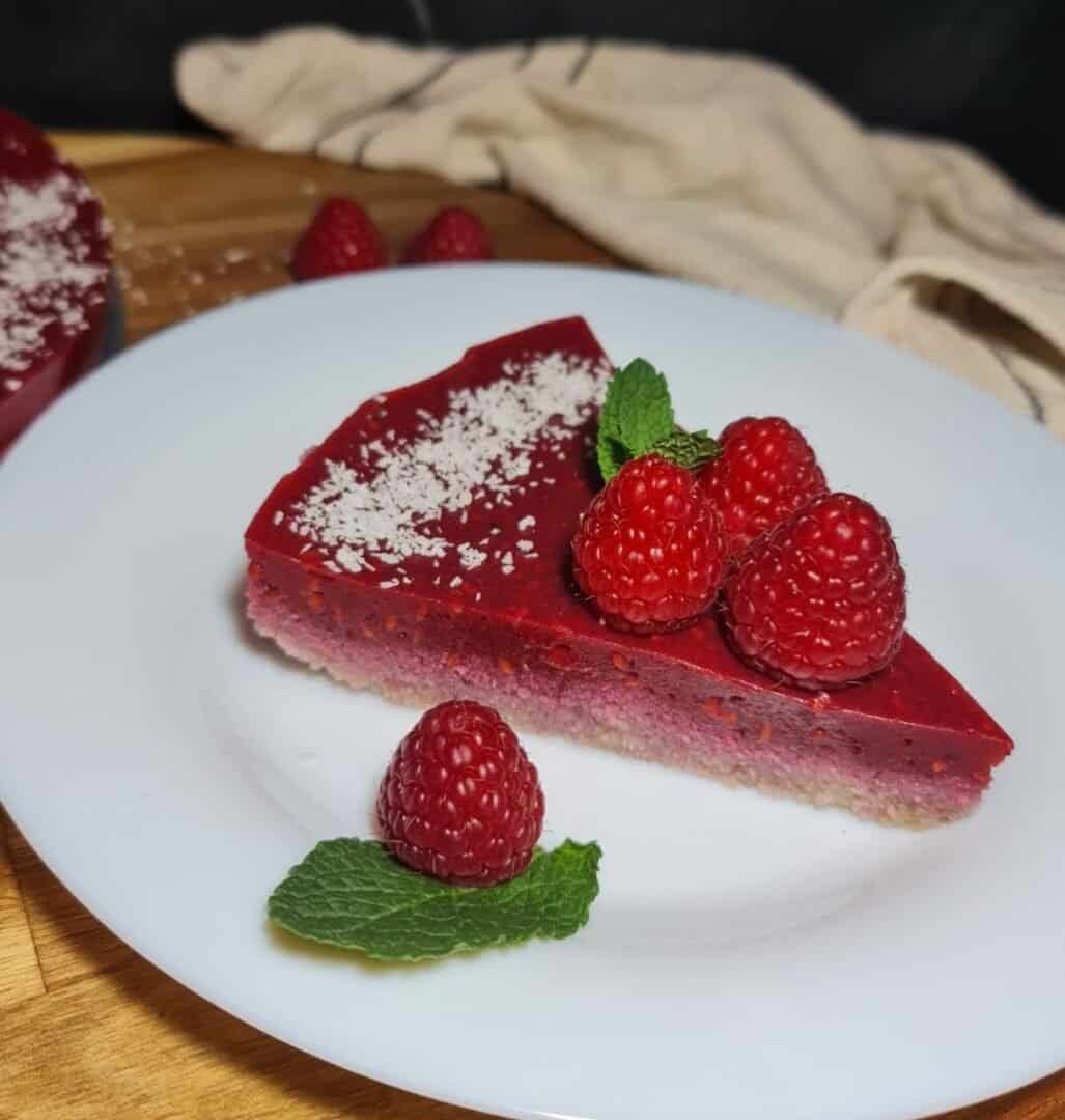 A slice of guilt-free raspberry cake garnished with fresh raspberries and mint leaves on a white plate.