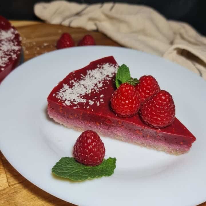 A slice of guilt-free raspberry cake garnished with fresh raspberries and mint leaves on a white plate.