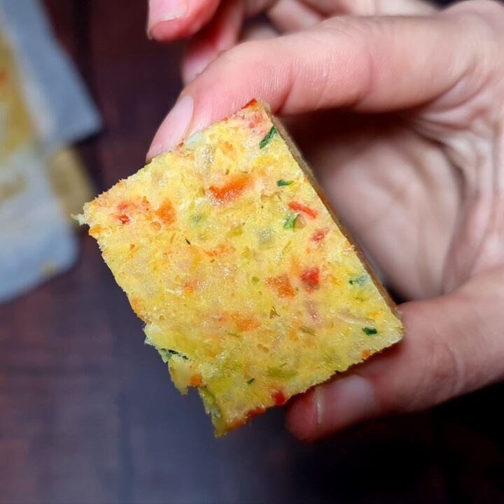 Close-up of a homemade vegetable broth cube held between fingers, showing a colorful mix of finely chopped vegetables.