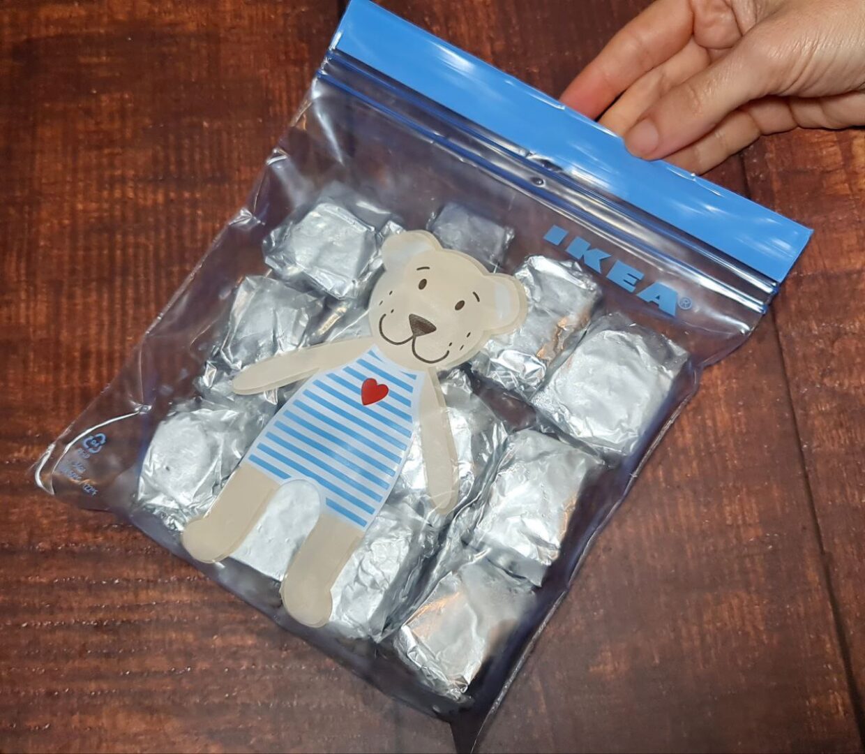 A hand holding an IKEA resealable bag containing homemade vegetable broth cubes wrapped in aluminum foil, with a bear illustration on the bag.