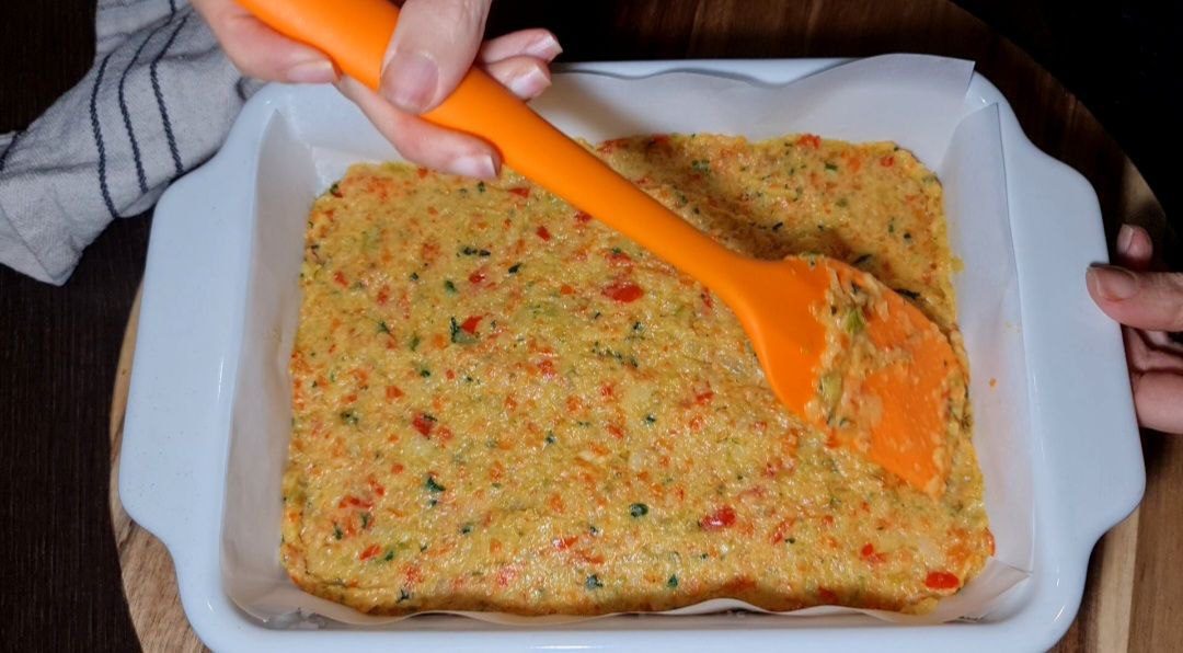 Spreading homemade vegetable broth mixture in a baking dish with an orange spatula.