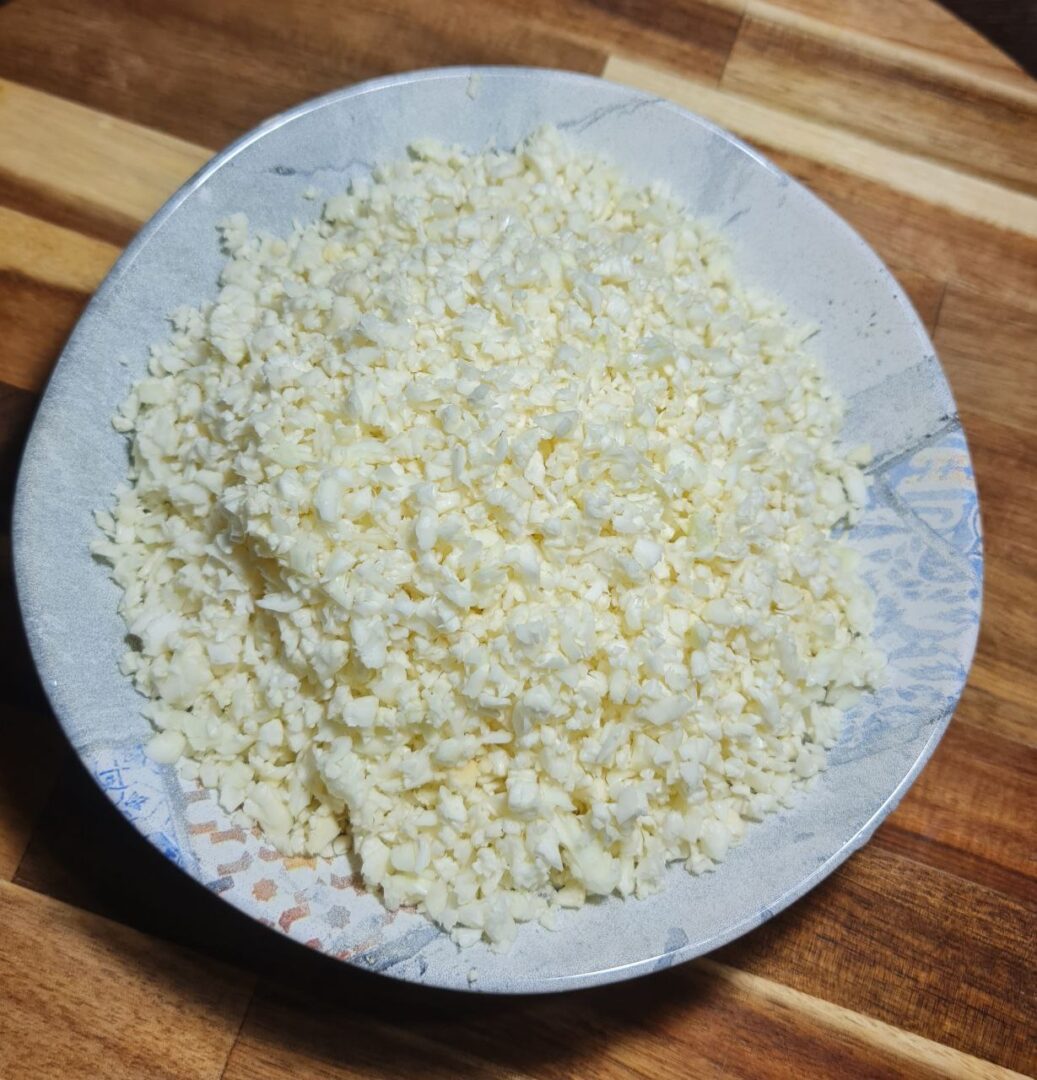 A plate filled with finely chopped cauliflower rice on a wooden surface.