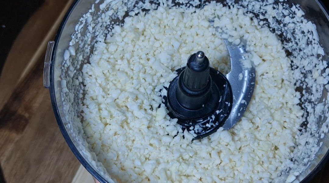 A food processor filled with finely chopped cauliflower, showing the process of making cauliflower rice.