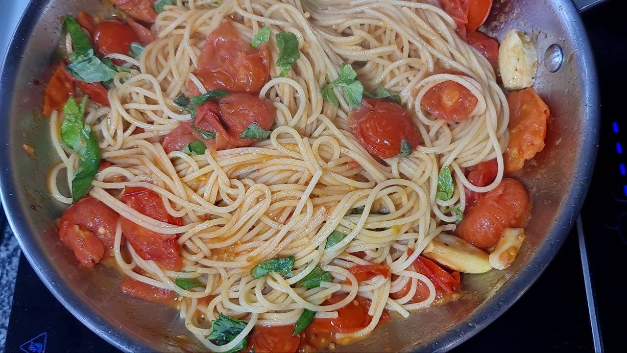 A pan of spaghetti pasta mixed with cherry tomatoes, fresh basil, and garlic cloves.