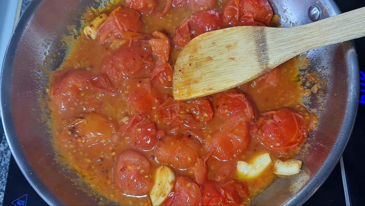 Cooking cherry tomatoes in a pan with garlic for a pasta sauce.