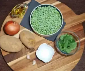 Bowl of frozen green peas, fresh mint, potatoes, onion, garlic, and olive oil on a wooden board